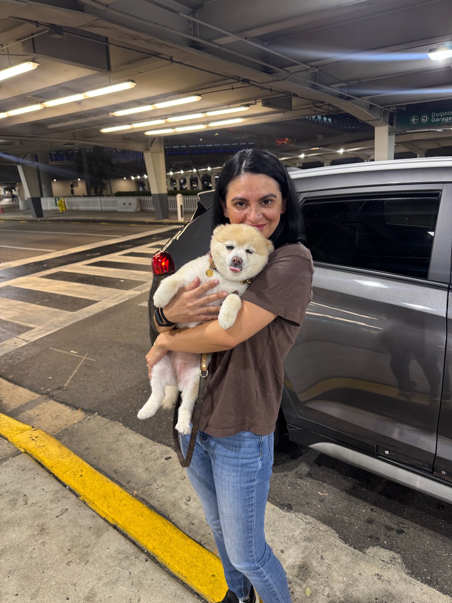 A woman welcoming a small white dog at an airport