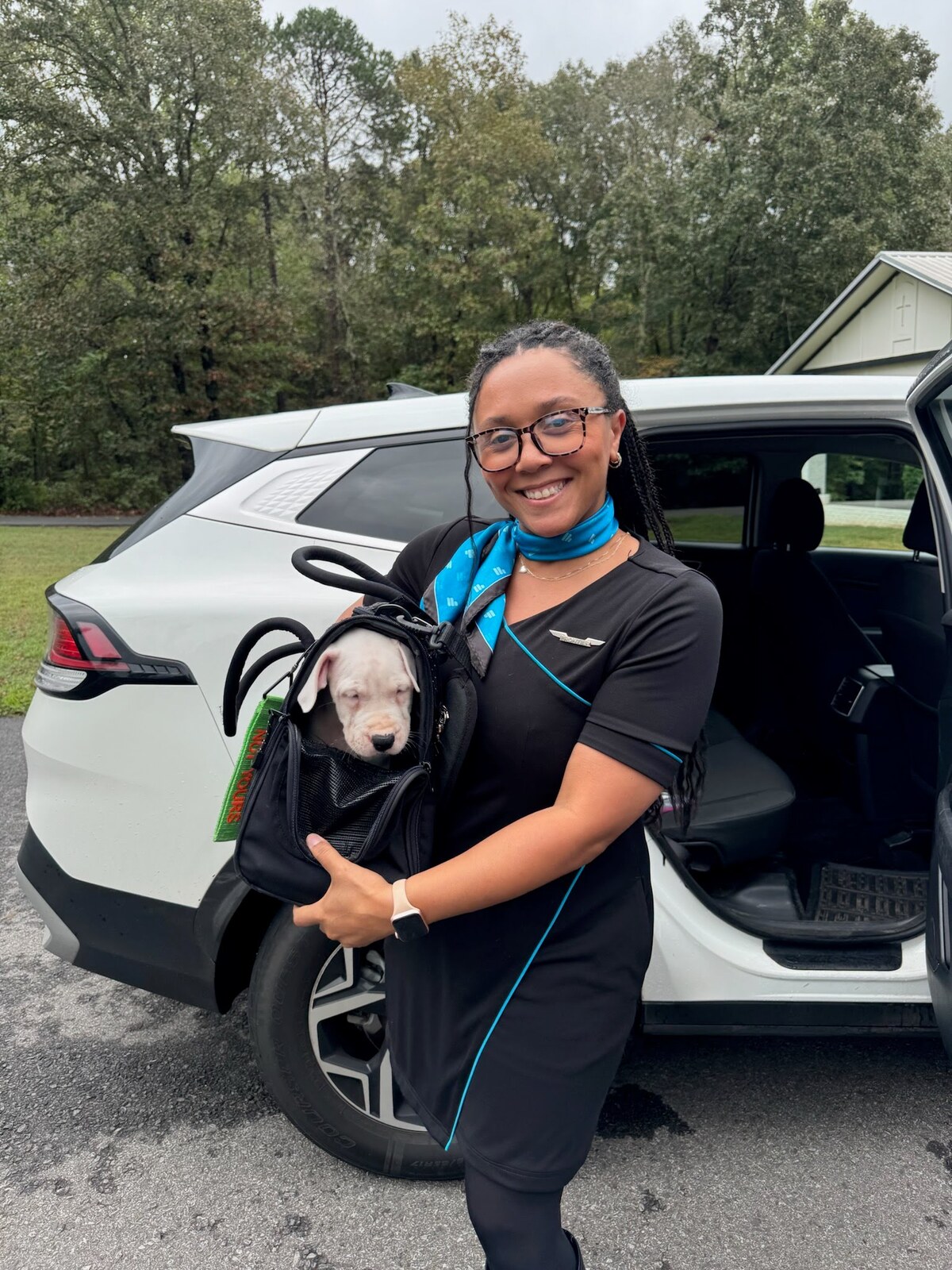 A flight nanny holding a small dog beside a vehicle
